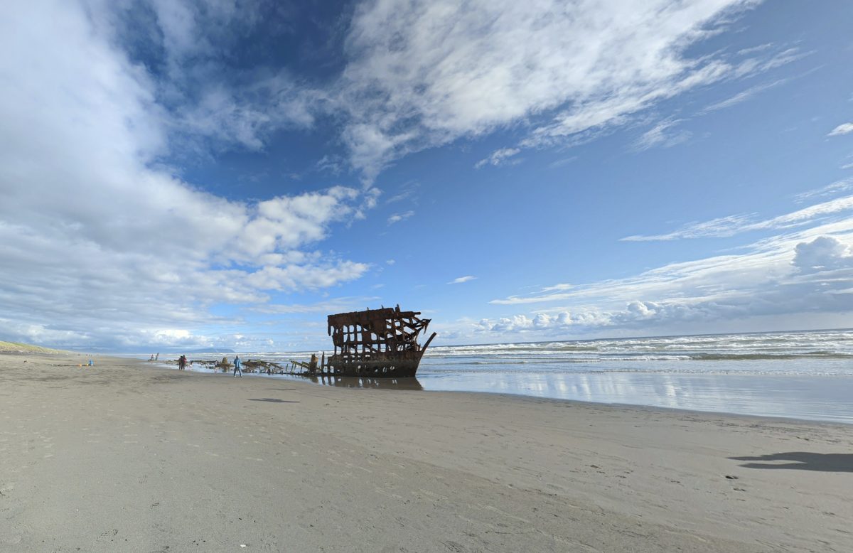 The rusted frame of the Peter Iredale shipwreck on a beach under a cloudy sky